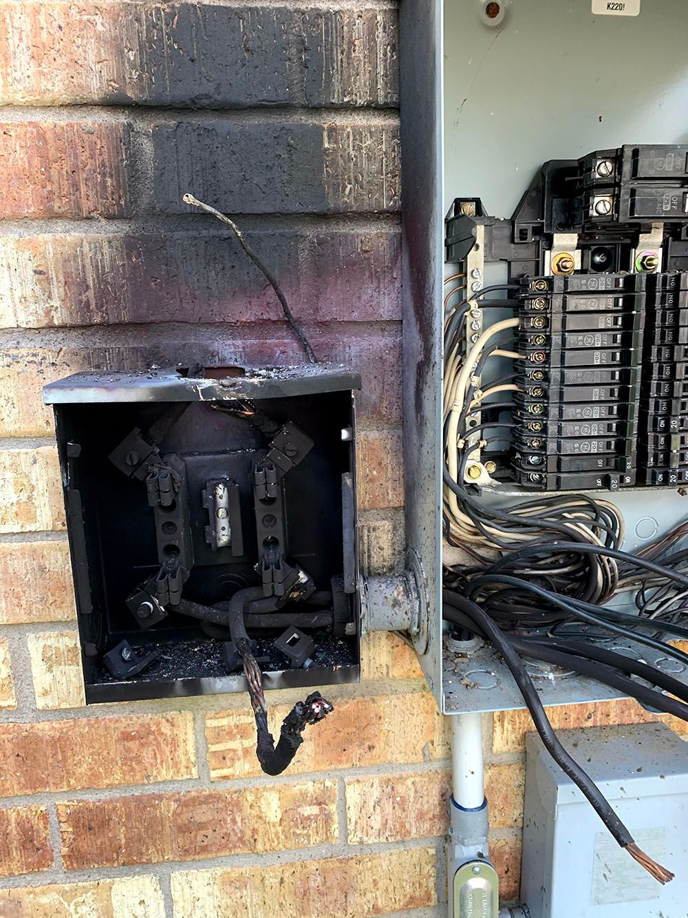 A damaged electrical box is sitting on a brick wall