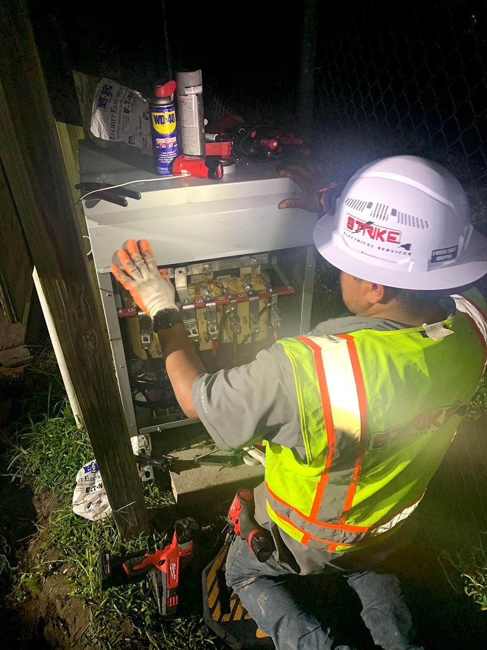 A man wearing a hard hat and safety vest is working on an electrical box
