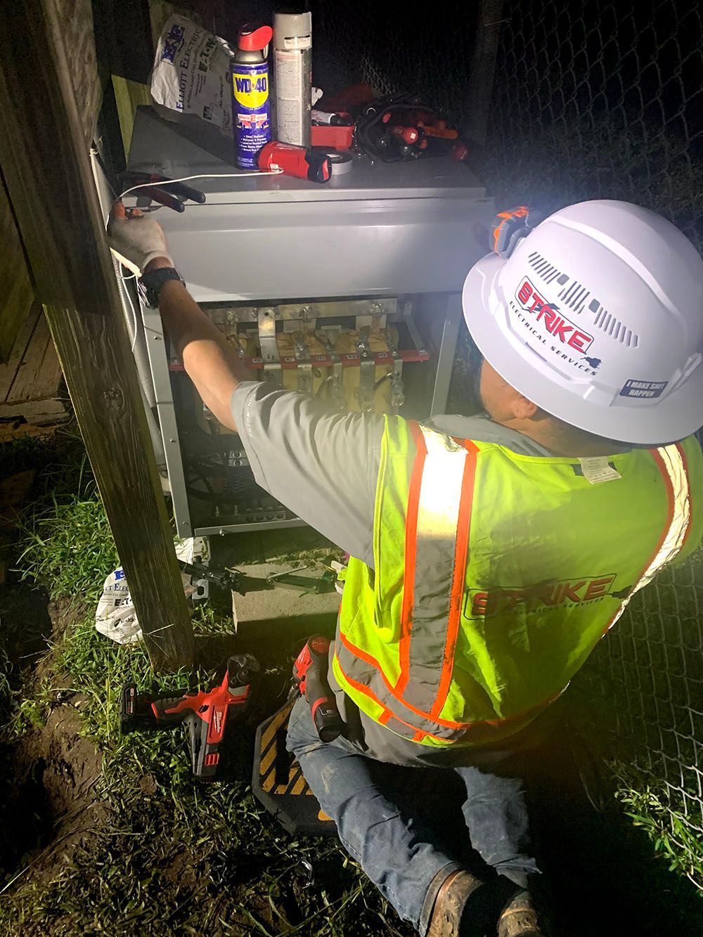 A man with a hard hat and safety vest is working on an electrical box