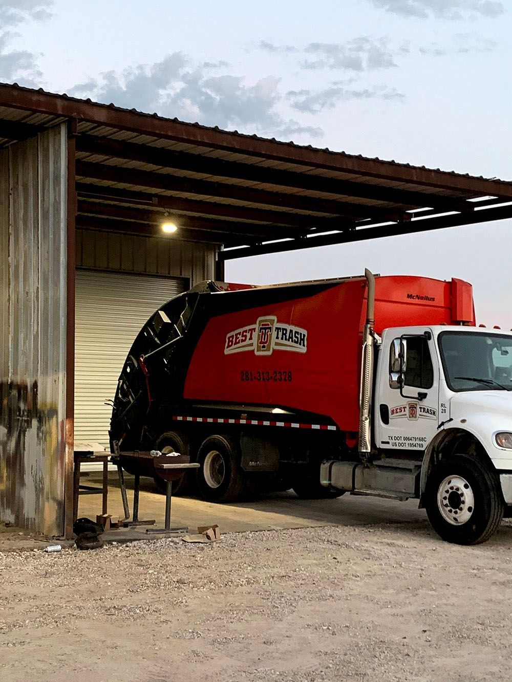 A red garbage truck is parked under a well-lighted garage