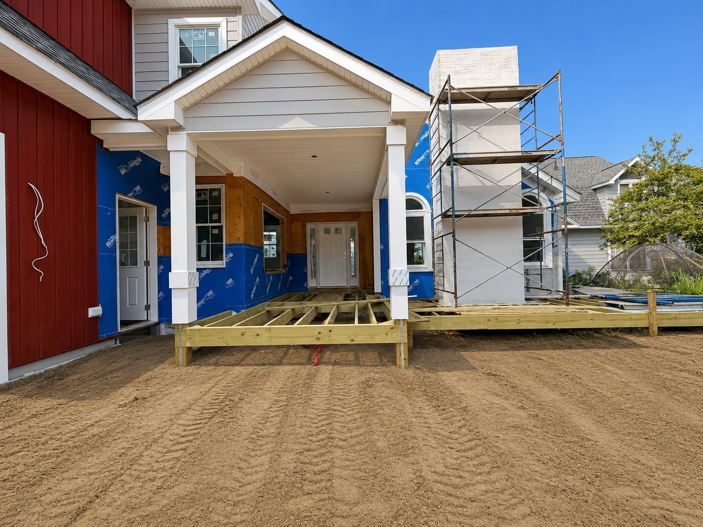 Front entrance of a house under construction with scaffolding, blue siding, and a fresh dirt yard