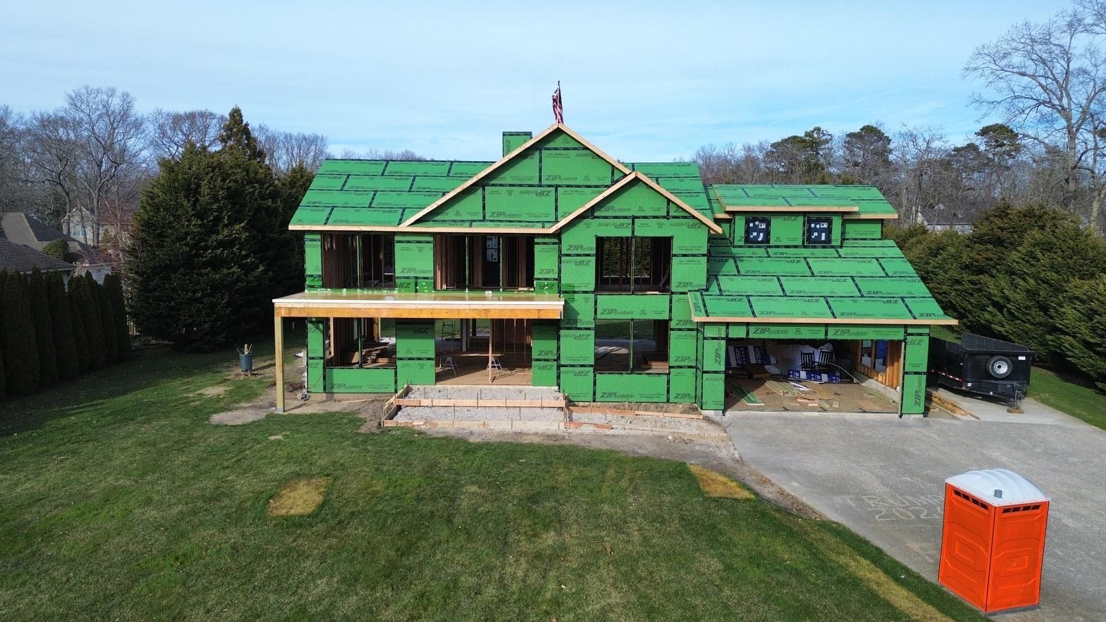 Large house with green roof and trim, front porch, driveway, and orange dumpster in the yard