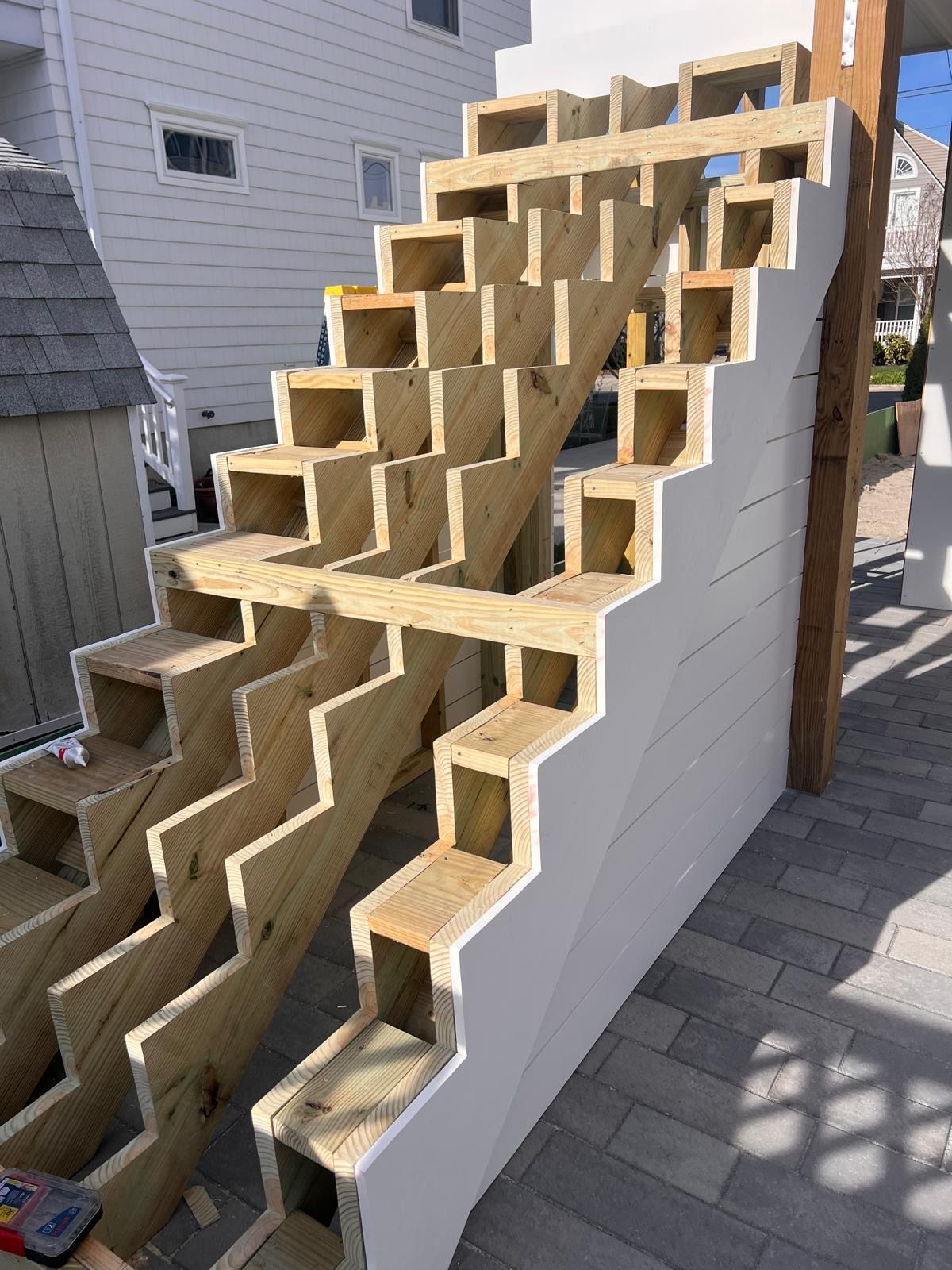 Wooden stair framework under construction beside a house, with staggered steps and white side panels.