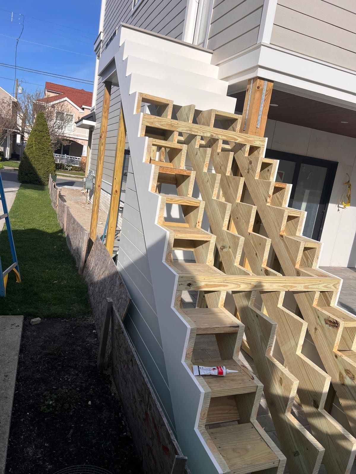 Wooden outdoor stairs under construction beside a house, with exposed framing and steps stacked along the side.