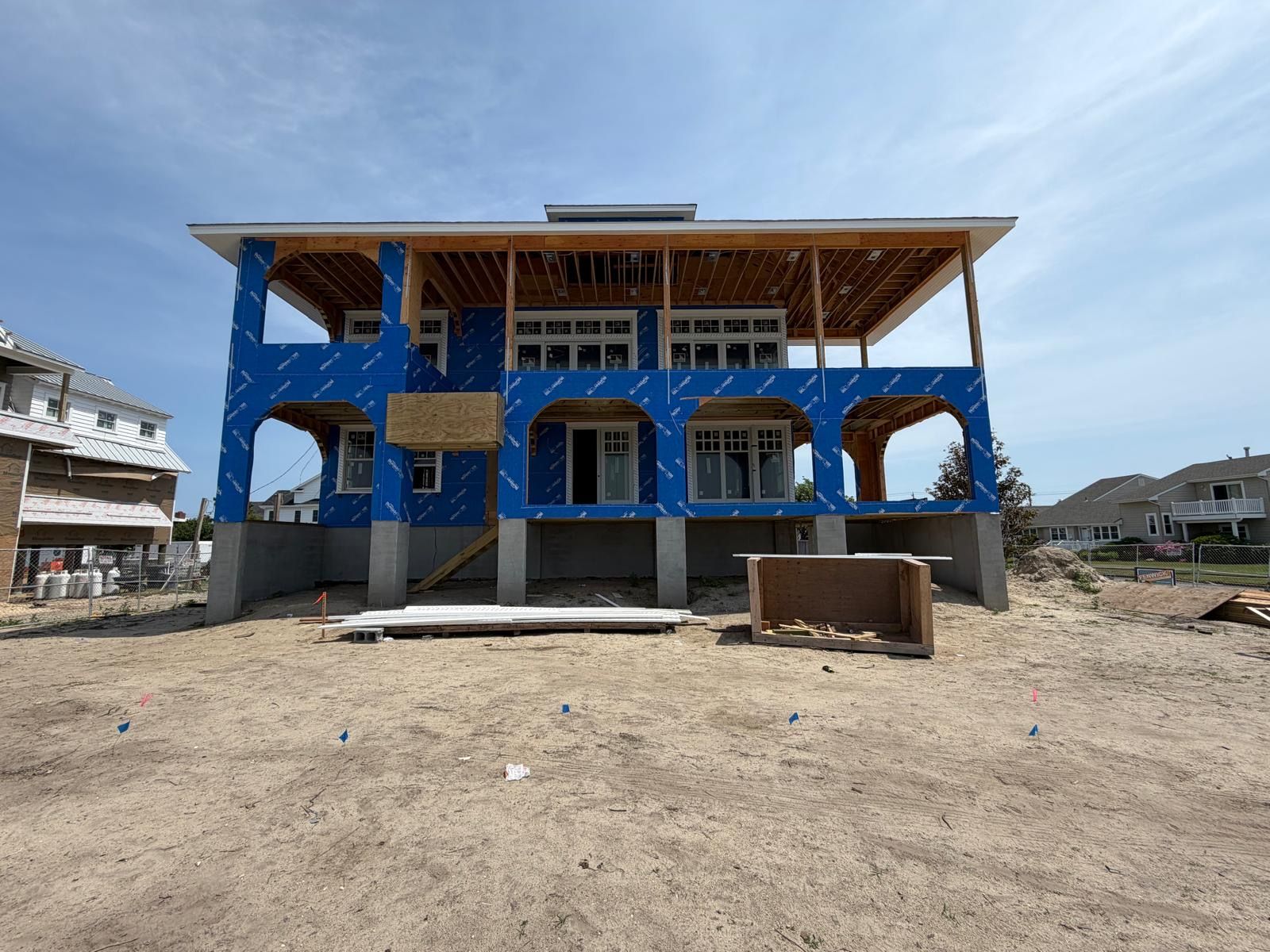 Blue house under construction with exposed framing on a sandy lot, viewed from the front.