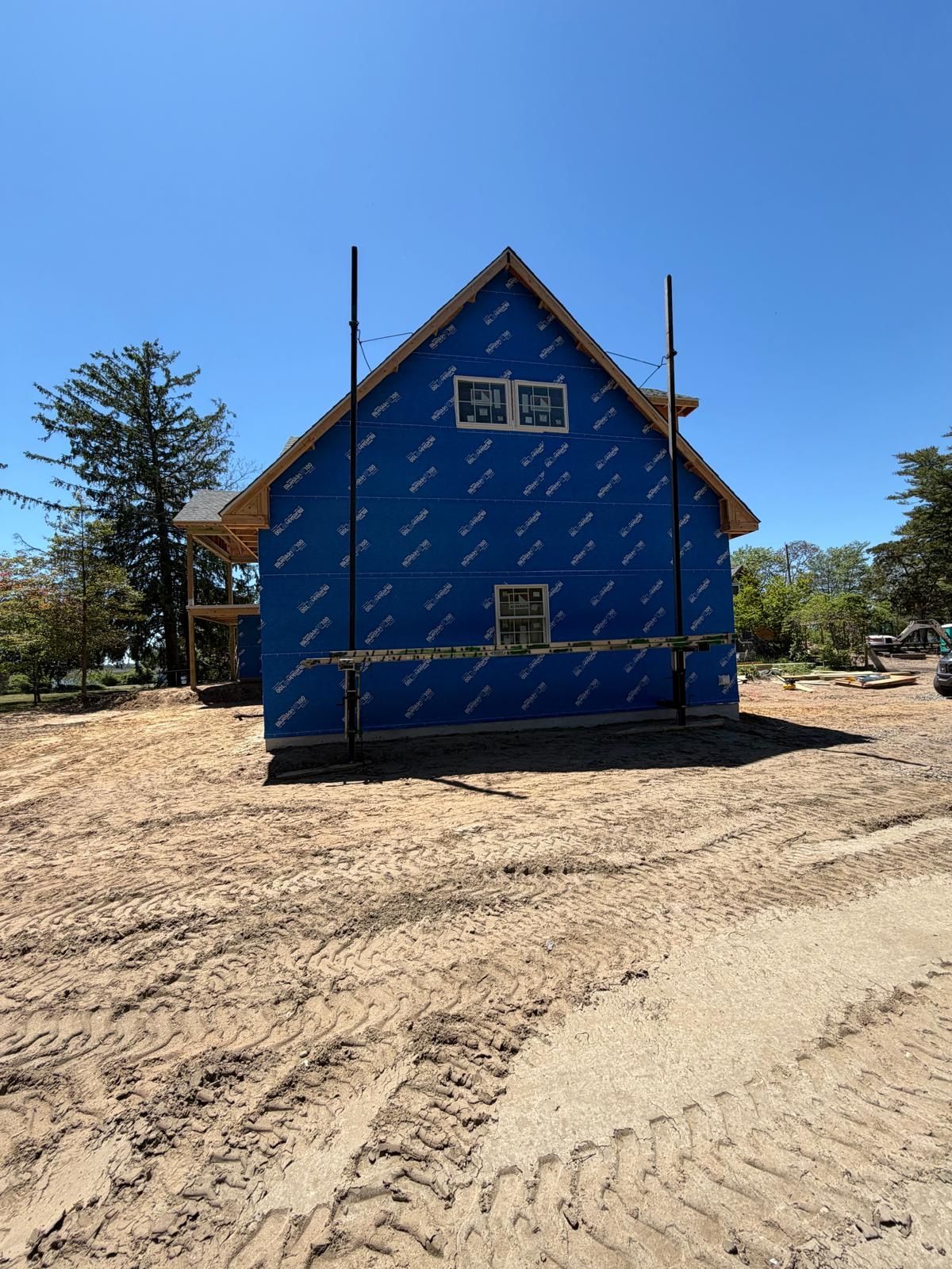 Blue house under construction with tarps and scaffolding on a dirt lot under a clear sky