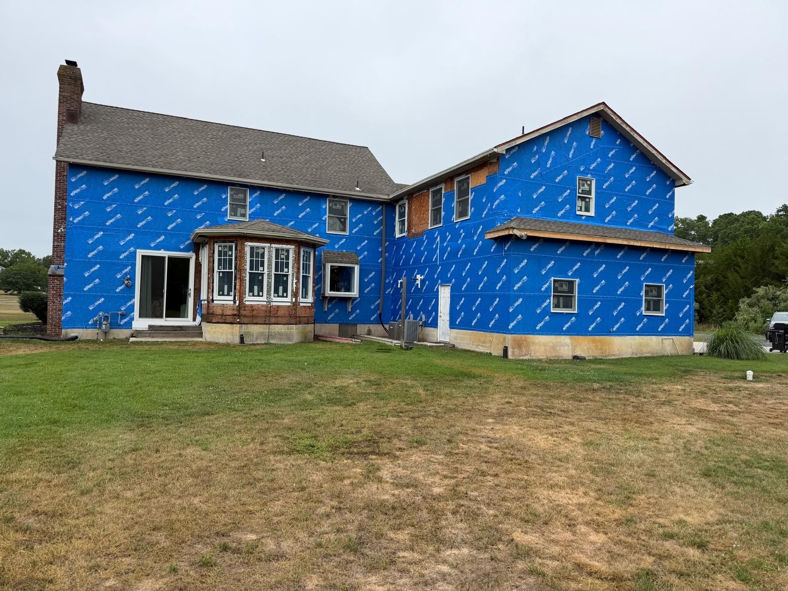 Blue two-story house under construction with exposed wrap and a grassy front yard