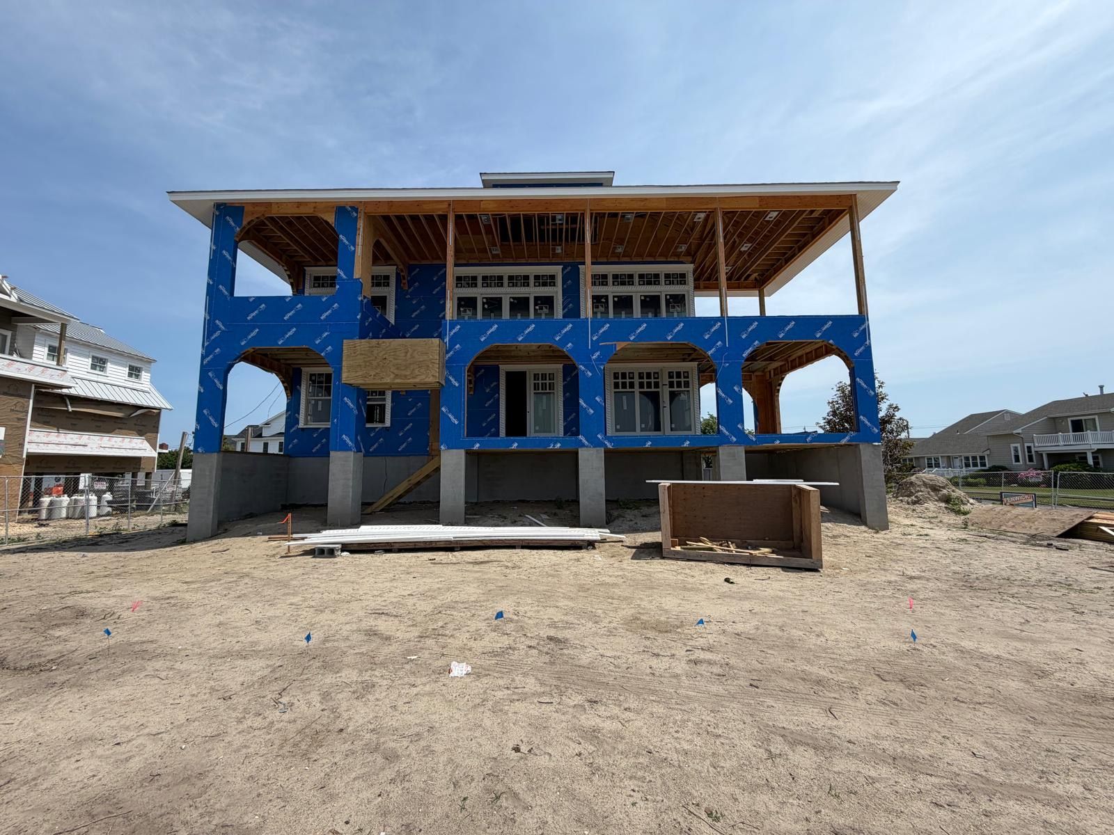Blue house under construction on a sandy lot, with exposed framing and unfinished porch.