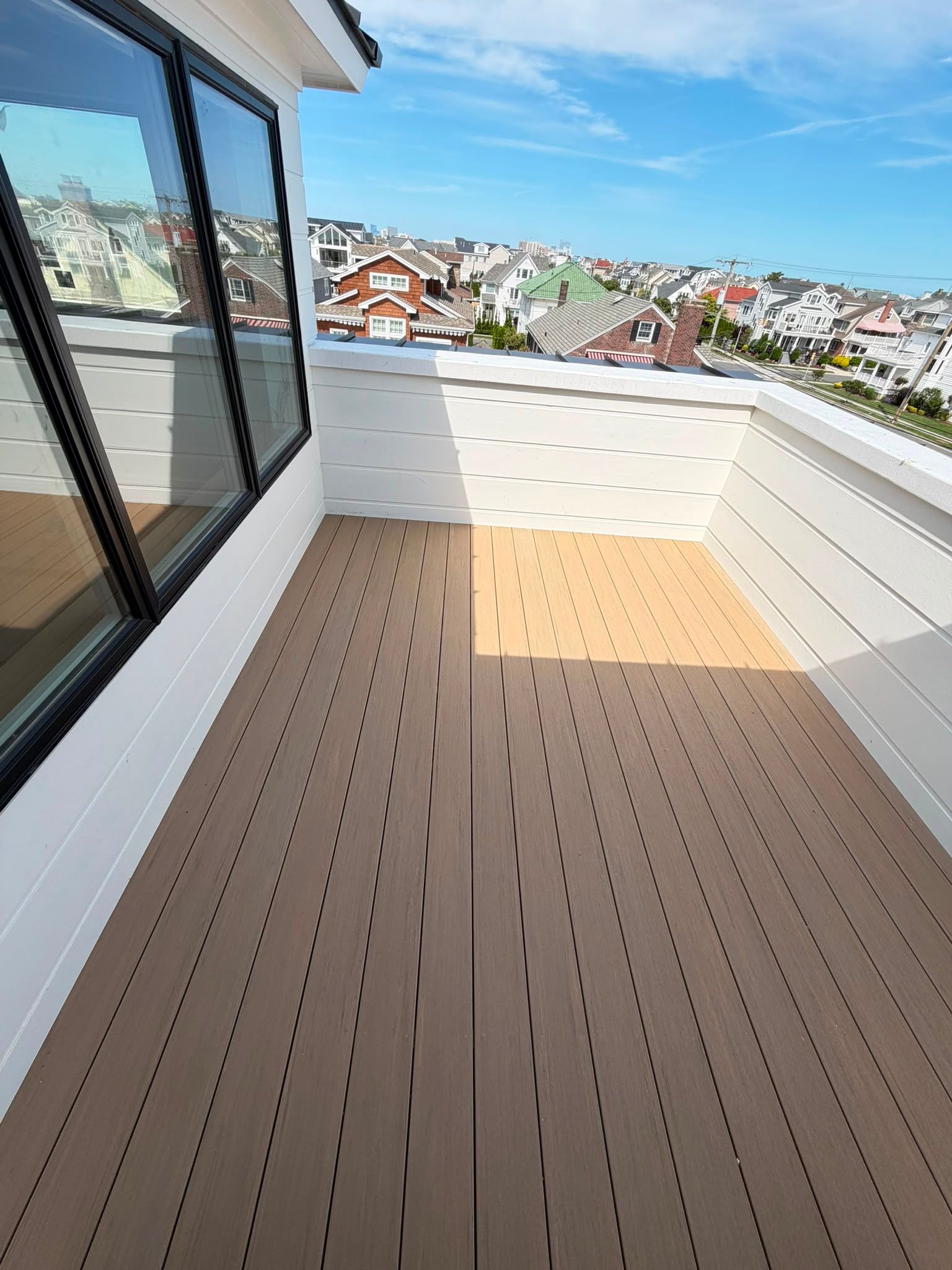 Empty rooftop balcony with wood-look decking, white railing, and city view under a blue sky