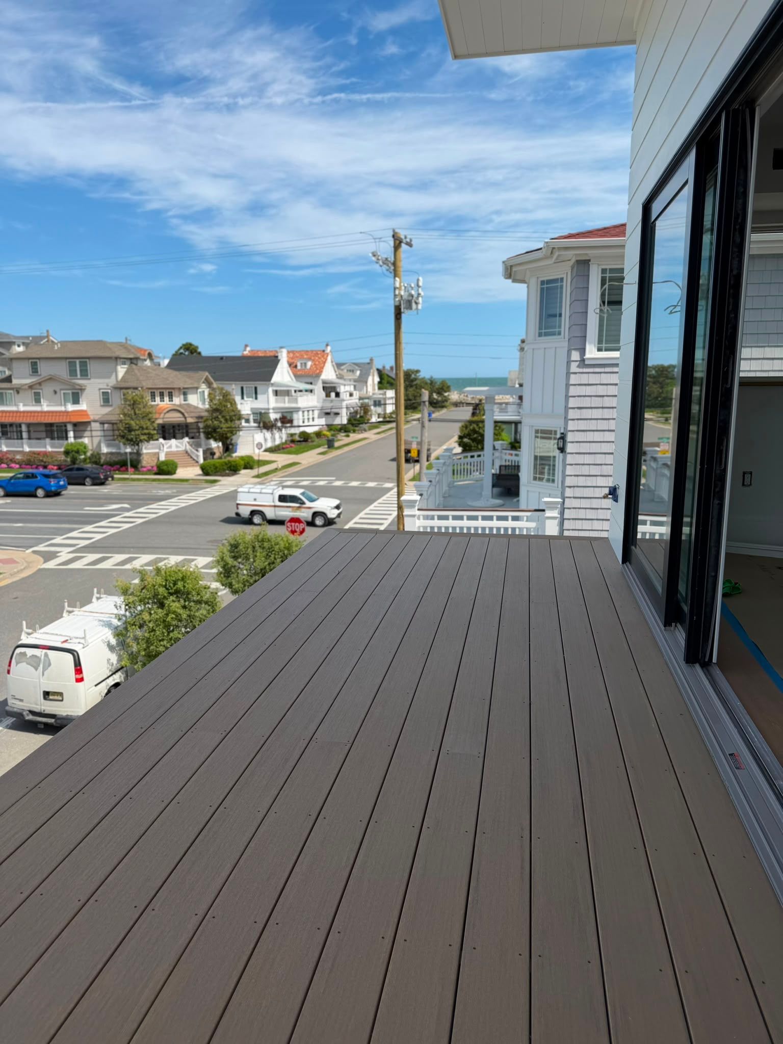 Balcony view of a sunny coastal street with parked cars, white houses, and blue sky
