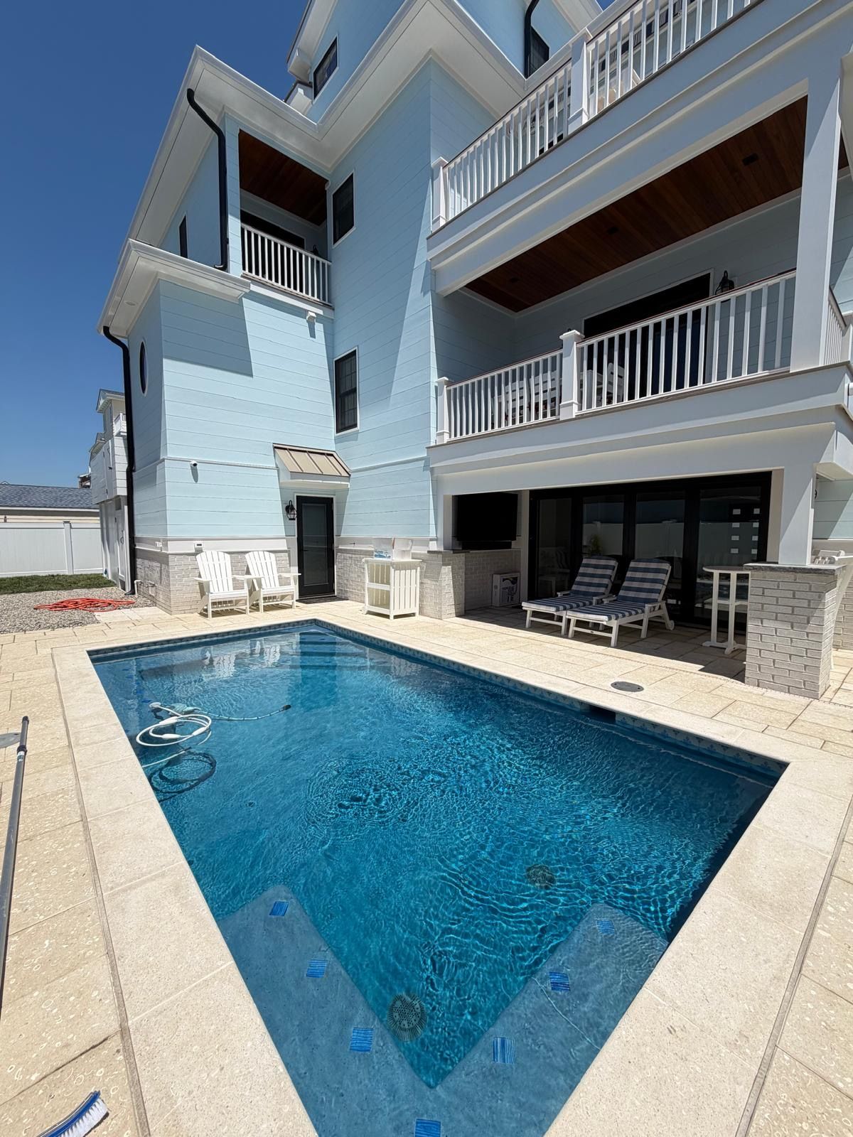 Blue swimming pool beside a light blue house with balconies and a shaded patio area