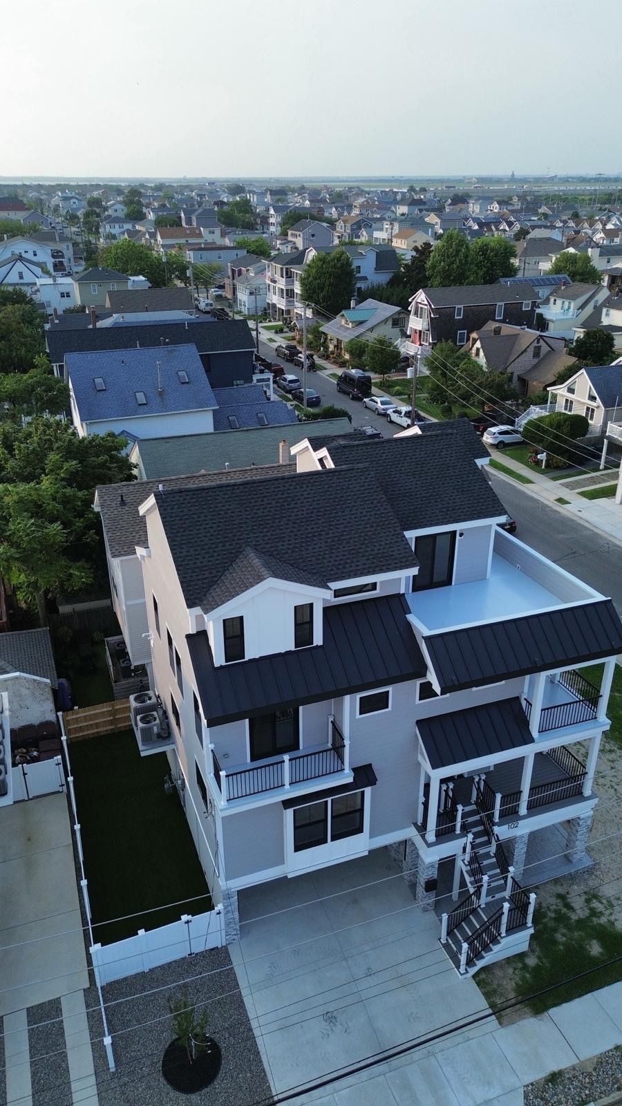 Aerial view of a modern white-and-gray house with a driveway in a suburban neighborhood.