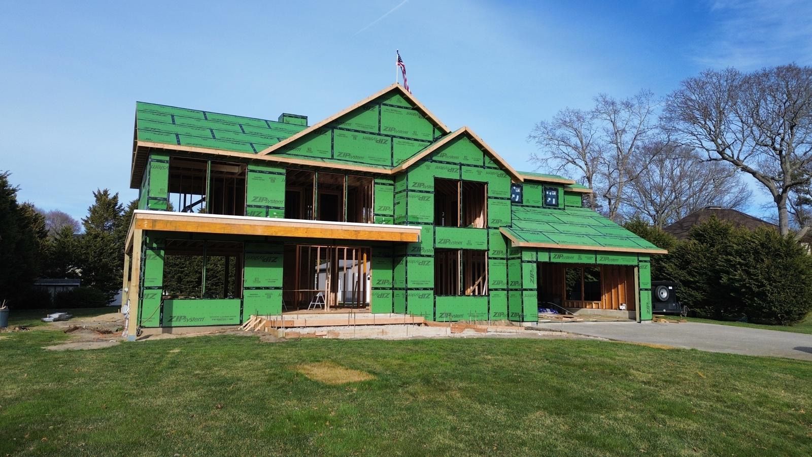 Green house under construction with exposed framing and a grassy yard in front