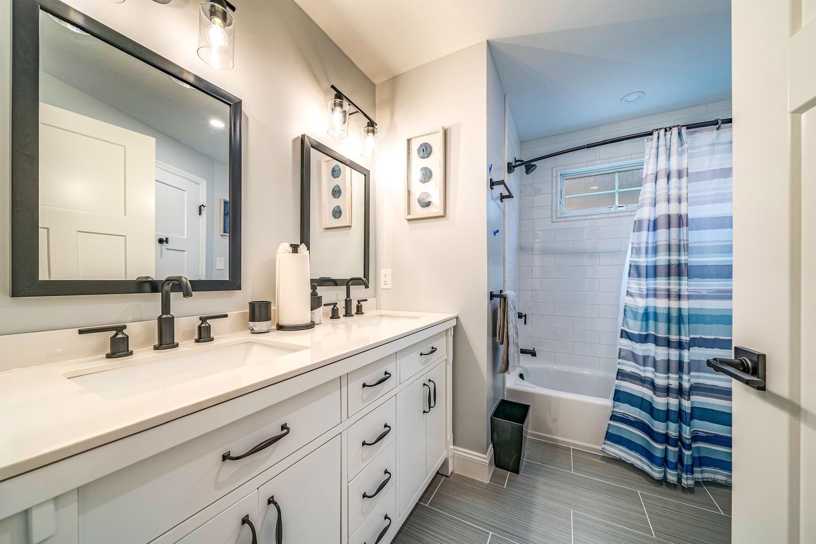 Bright bathroom with double vanity, large mirror, and blue-striped shower curtain.