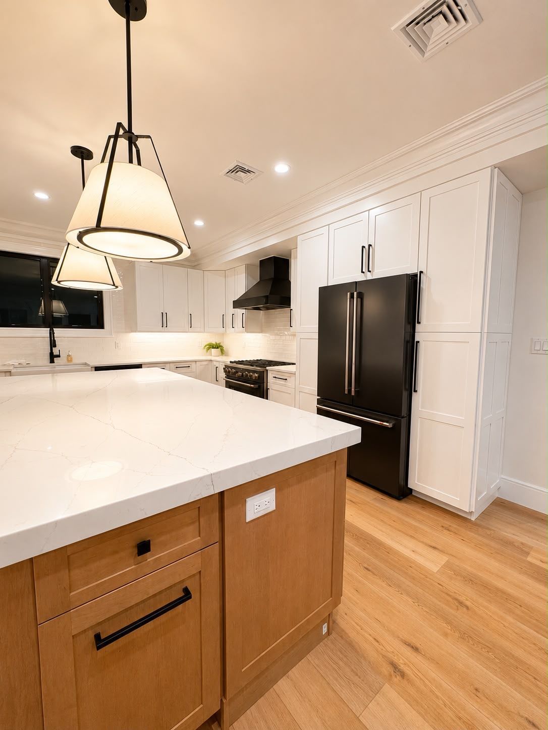 Bright white kitchen with island, pendant light, wood floors, and black refrigerator