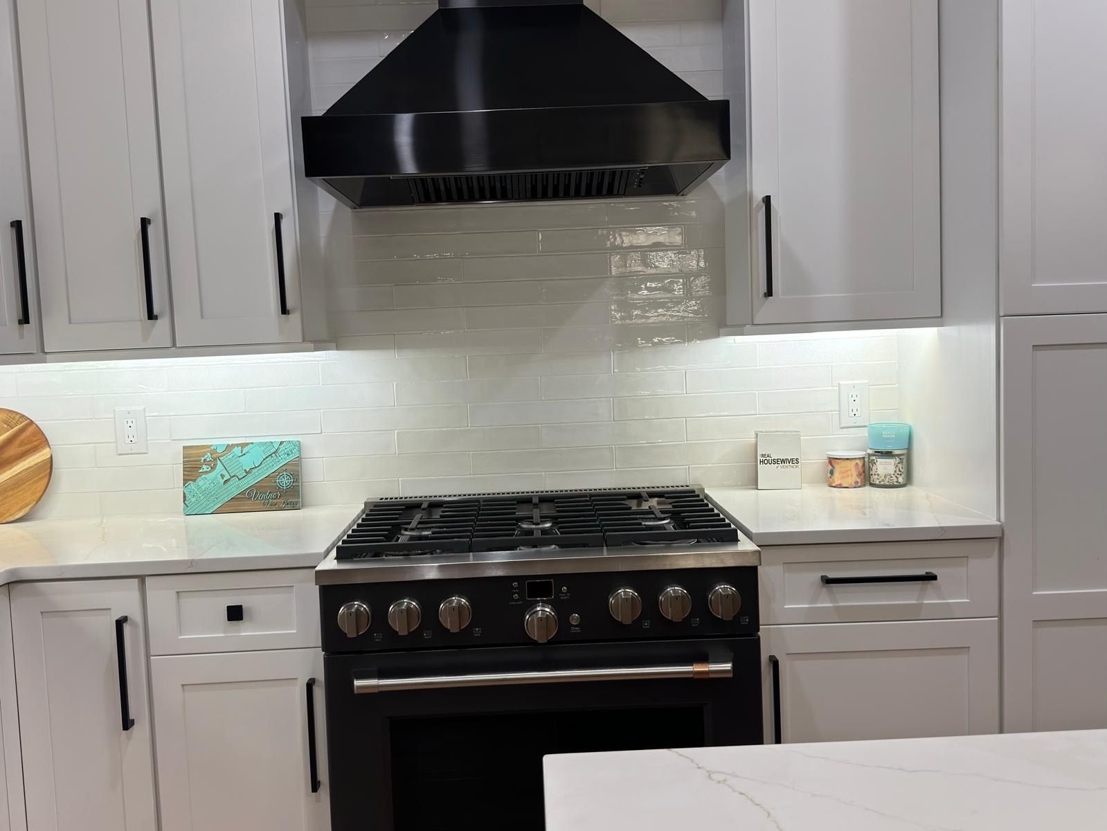 Modern white kitchen with black stove, range hood, and light backsplash cabinets