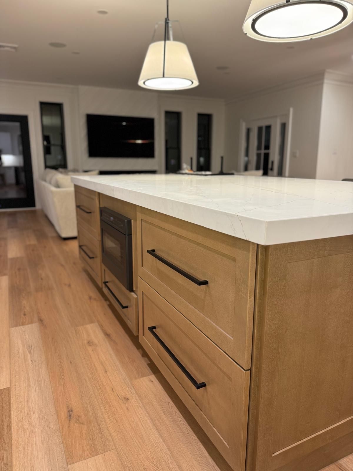 Modern kitchen with a large white island, wood cabinets, pendant lights, and wood flooring.