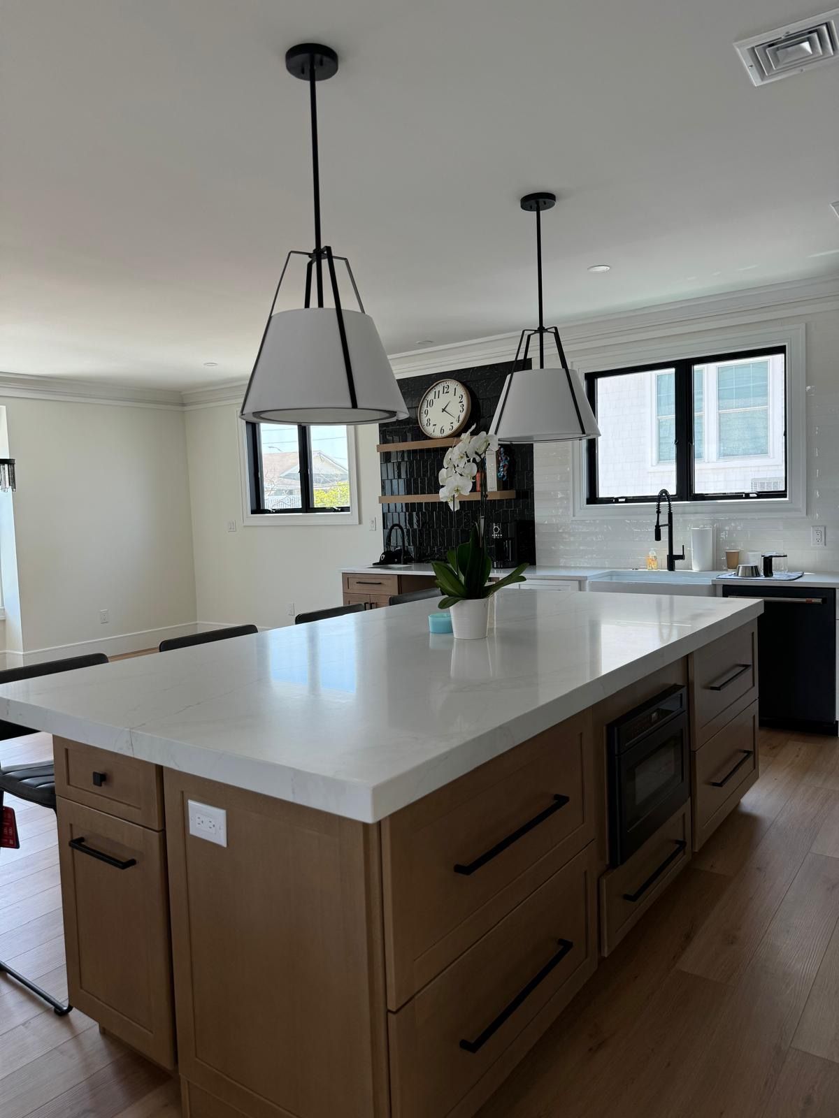 Modern kitchen with a large white island, pendant lights, wood floors, and a sink by the window.