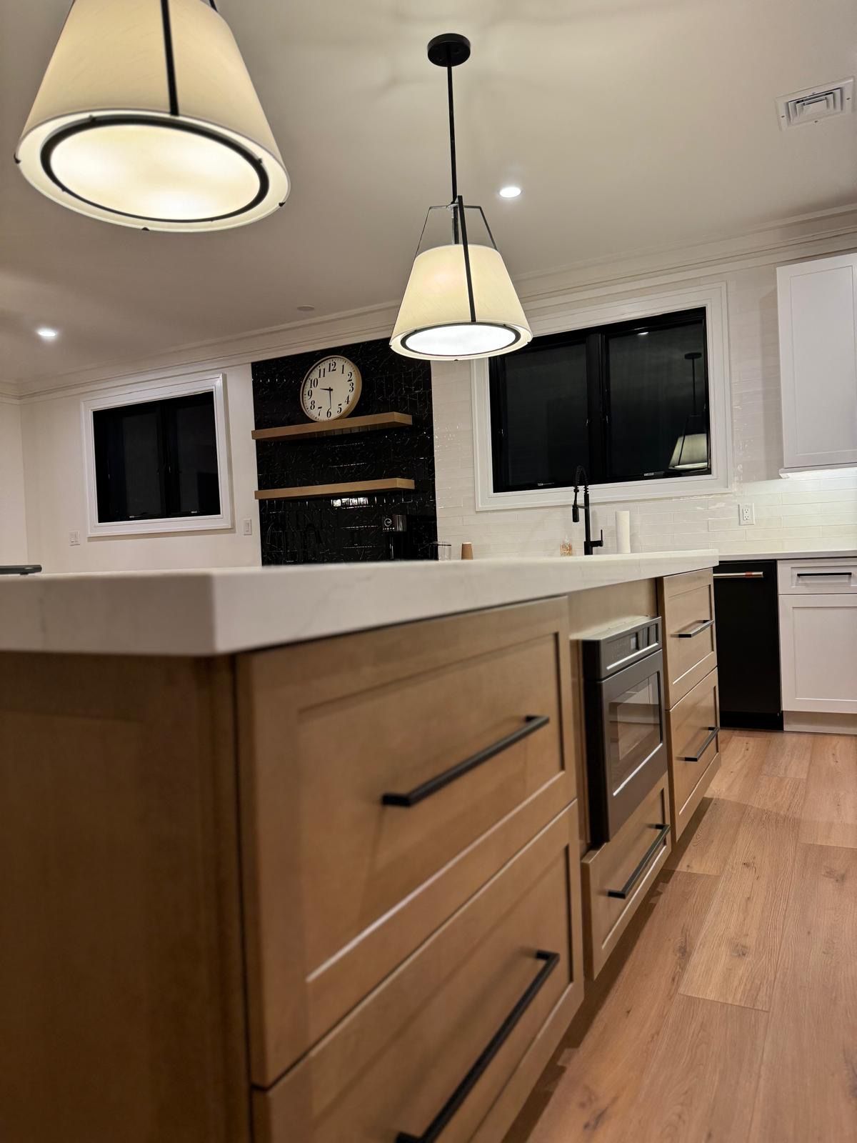 Modern kitchen with wood cabinets, white countertops, pendant lights, and black windows.