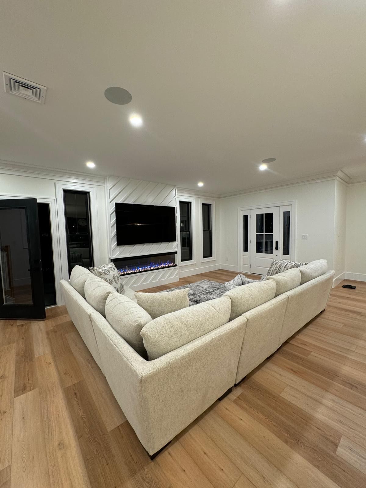 Spacious living room with a large cream sectional, wood floors, white walls, and a wall-mounted TV.