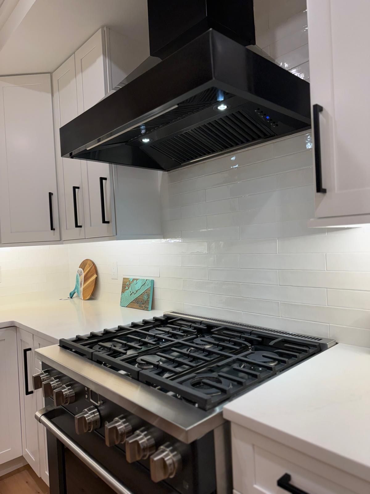 Modern kitchen with gas range, black hood, white cabinets, and white subway tile backsplash
