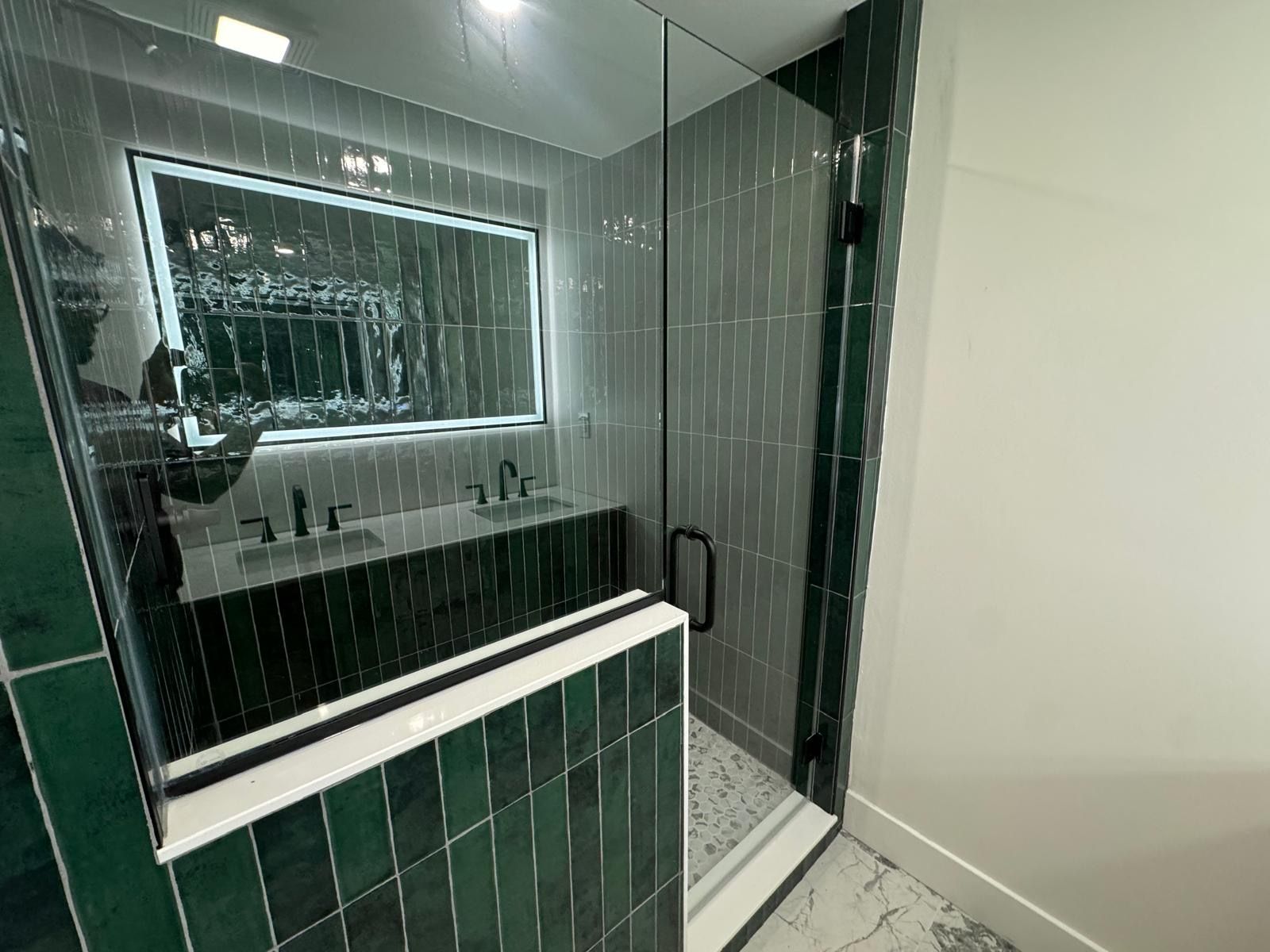 Modern bathroom with green tile, glass shower enclosure, and large mirror over a sink