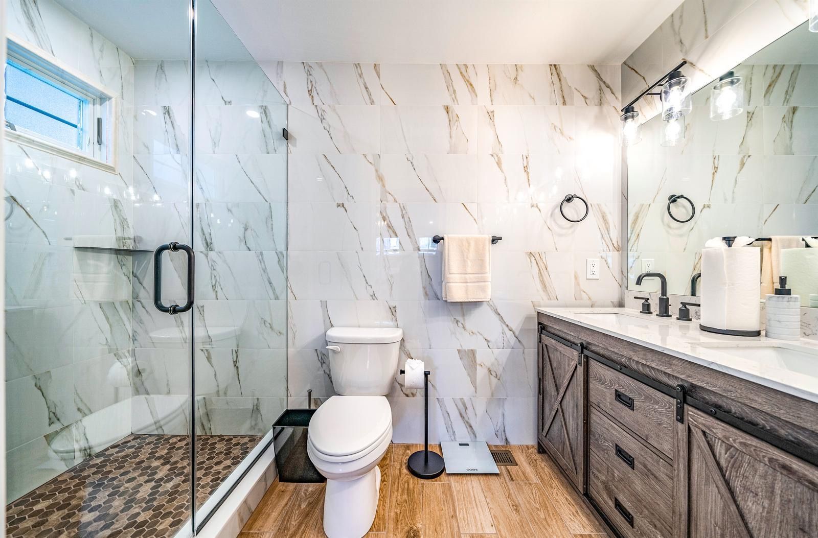 Modern bathroom with glass shower, toilet, marble walls, and dark wood vanity