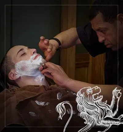 Barber shaving a person's face with a straight razor. Creamy lather covers the face, in a barbershop setting.