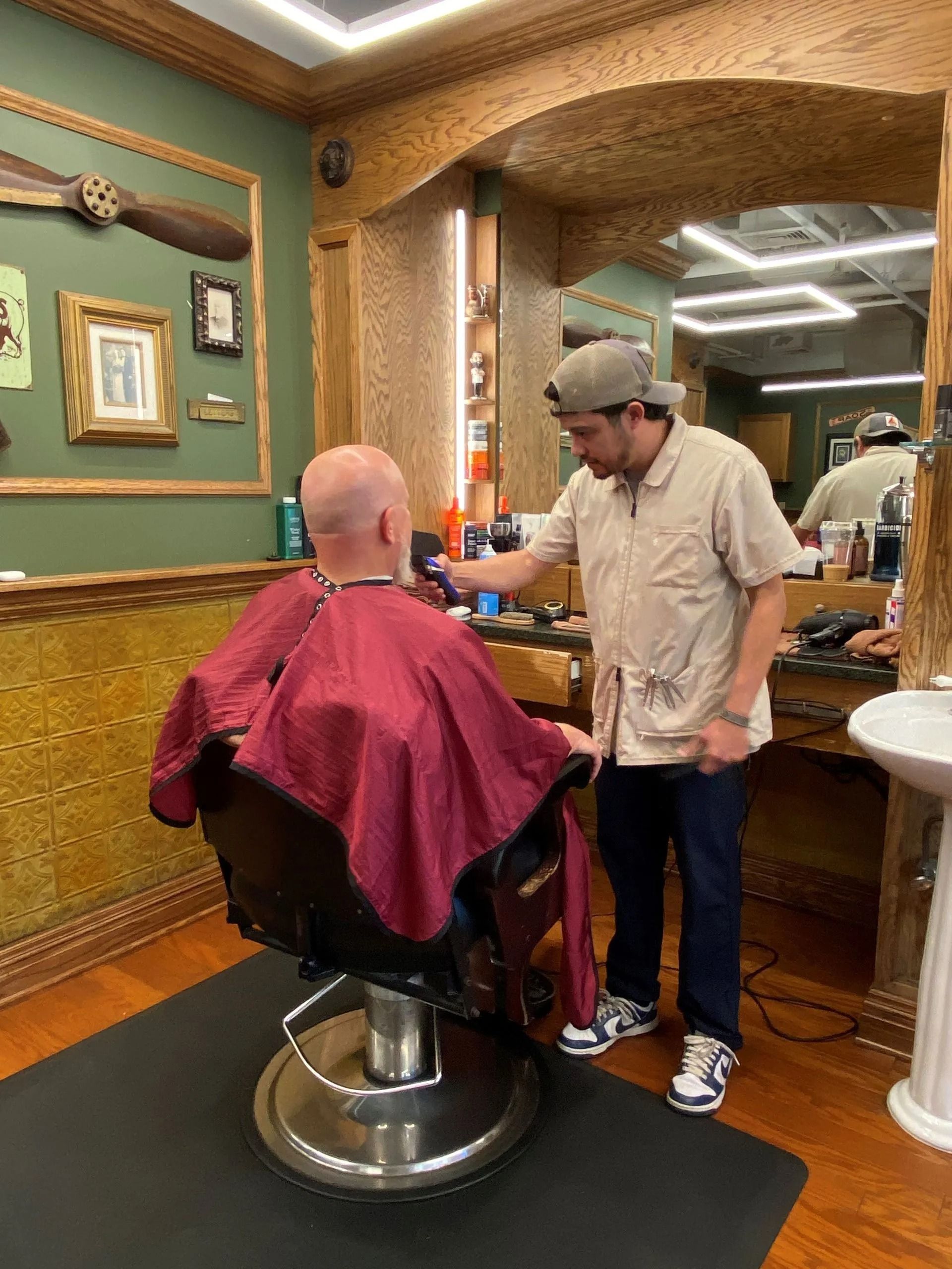 A barber giving a haircut to a client in a vintage-style barbershop. The barber is using clippers.