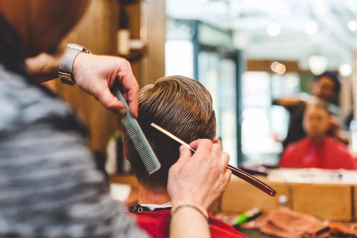 Barber using comb and straight razor to cut hair in a barbershop.