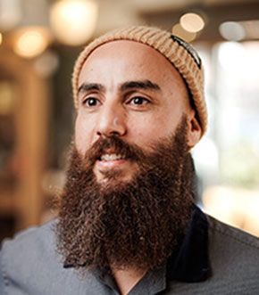 Man with a large beard and a tan beanie looking to the side with a slight smile.