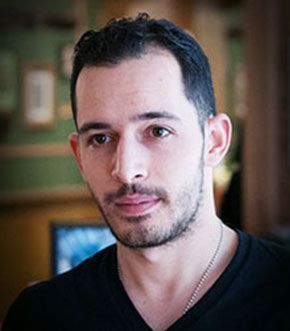 Man with dark hair and a light beard, wearing a black shirt, looking at the camera.