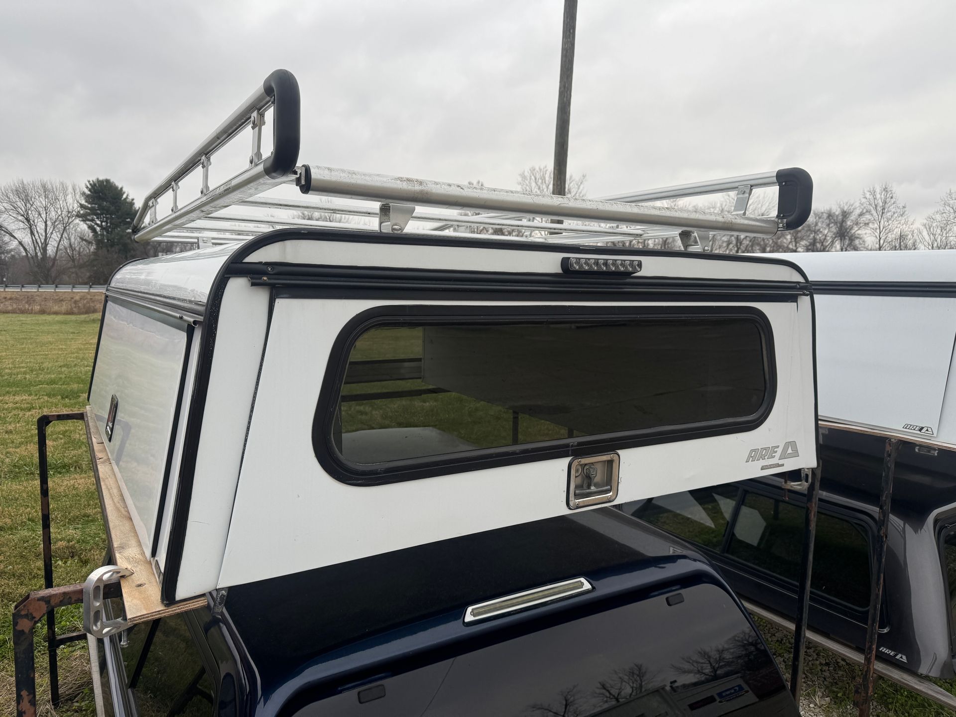White truck bed cap with ladder rack; parked outside.