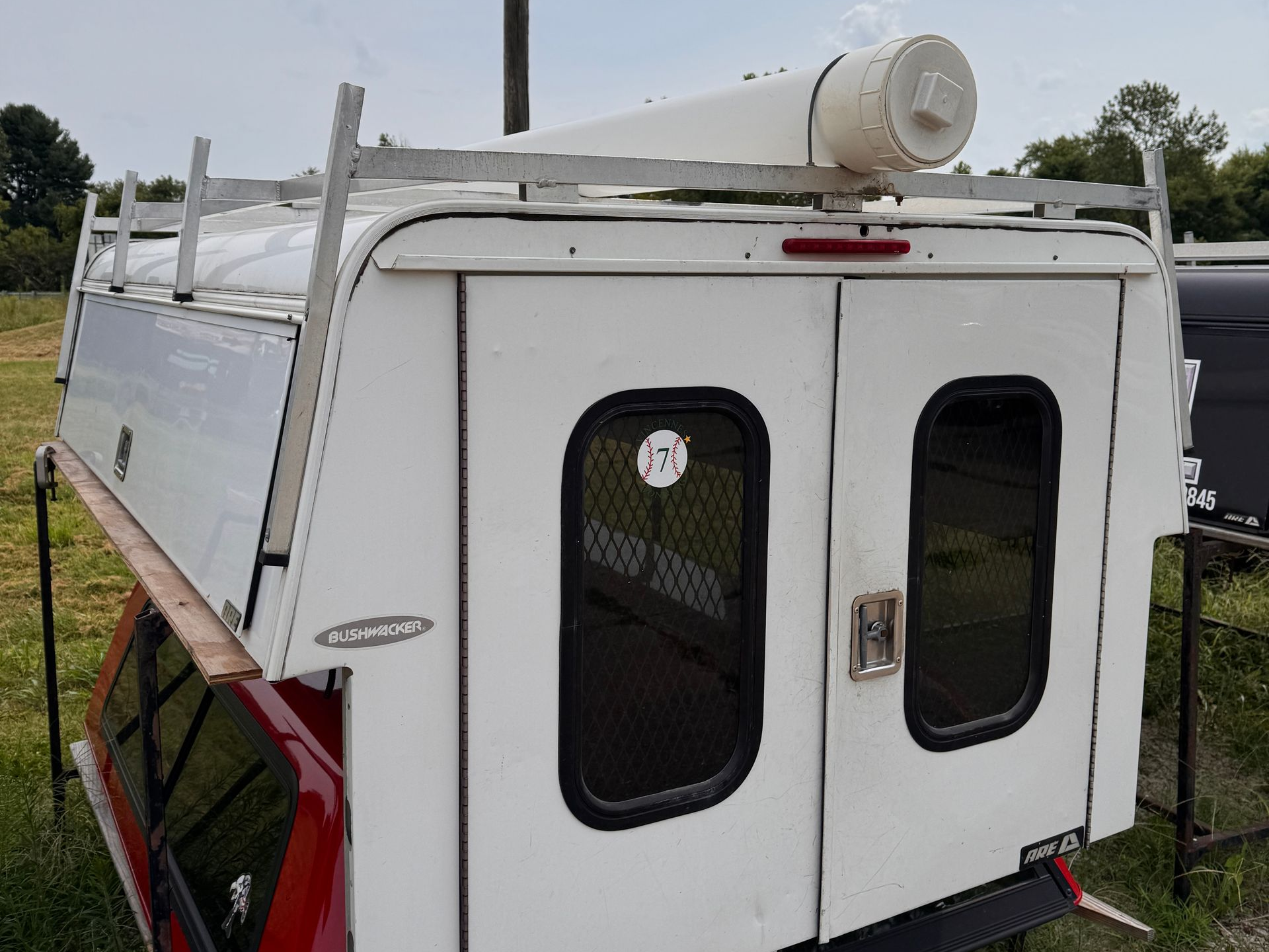 White rooftop camper shell with ladder and roof vent, viewed from the side on a truck.