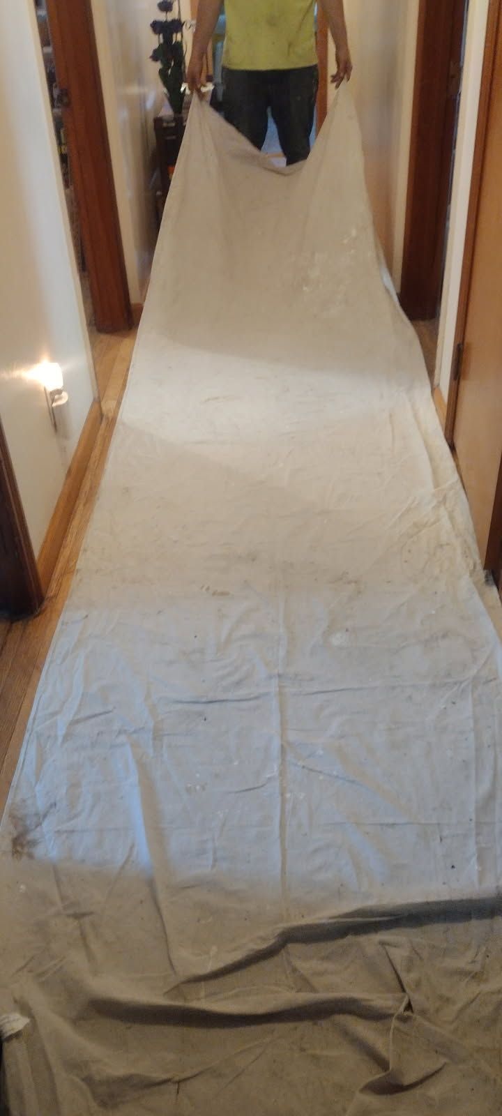 A person is holding a large white sheet in a hallway.