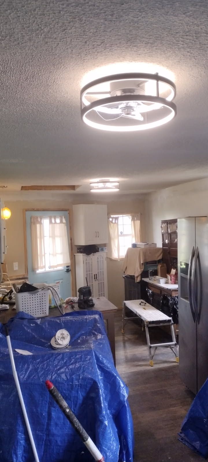 A living room with a blue tarp on the floor and a ceiling light.