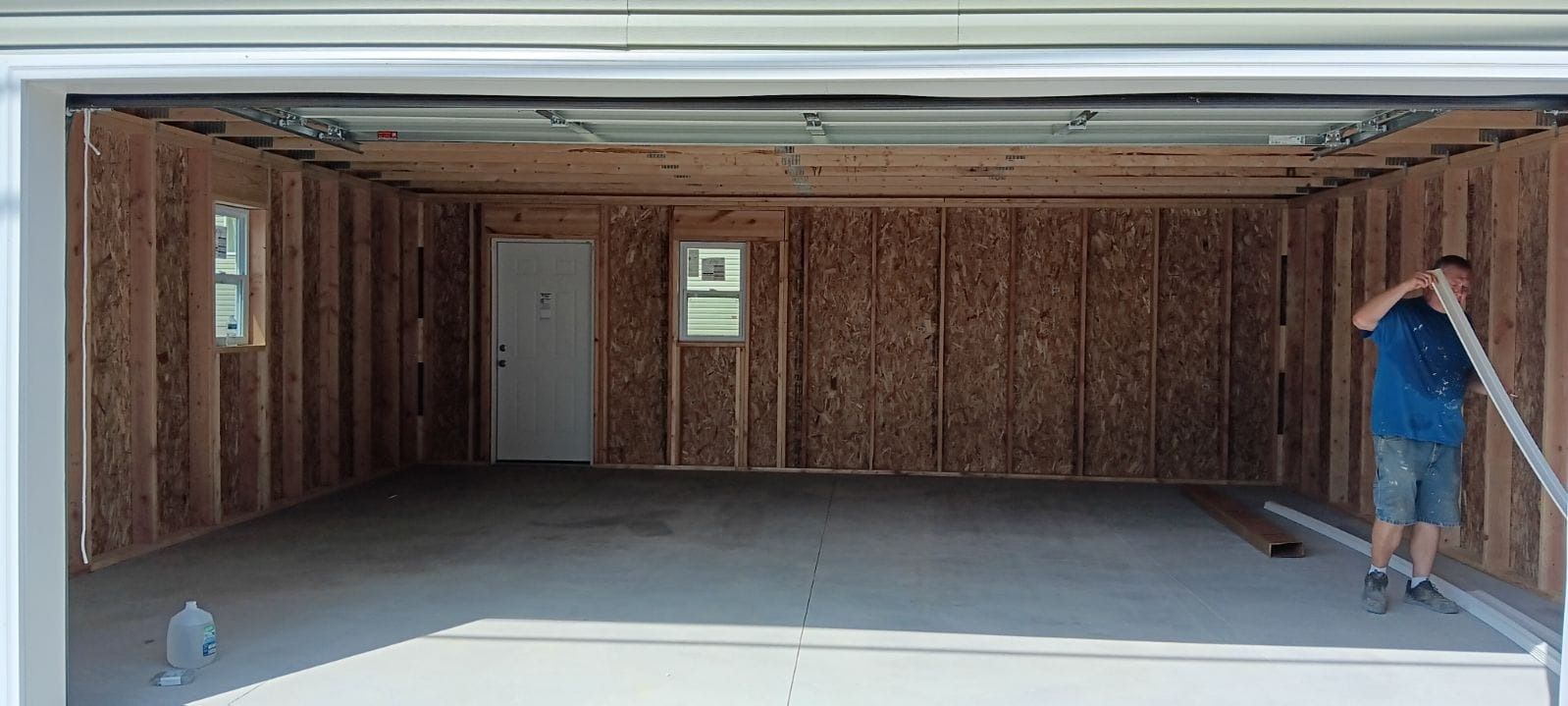 A man is standing in an empty garage with the door open.