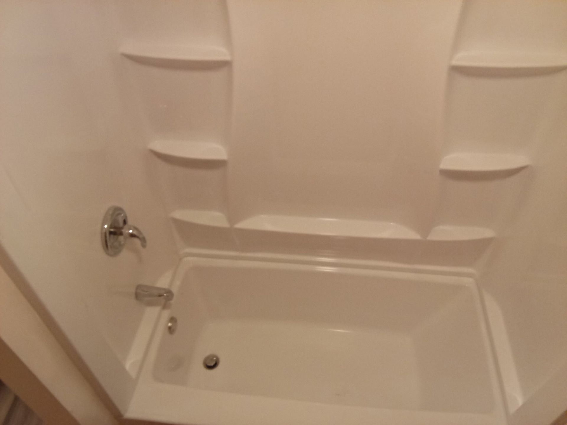 A white bathtub with shelves and a shower head in a bathroom.