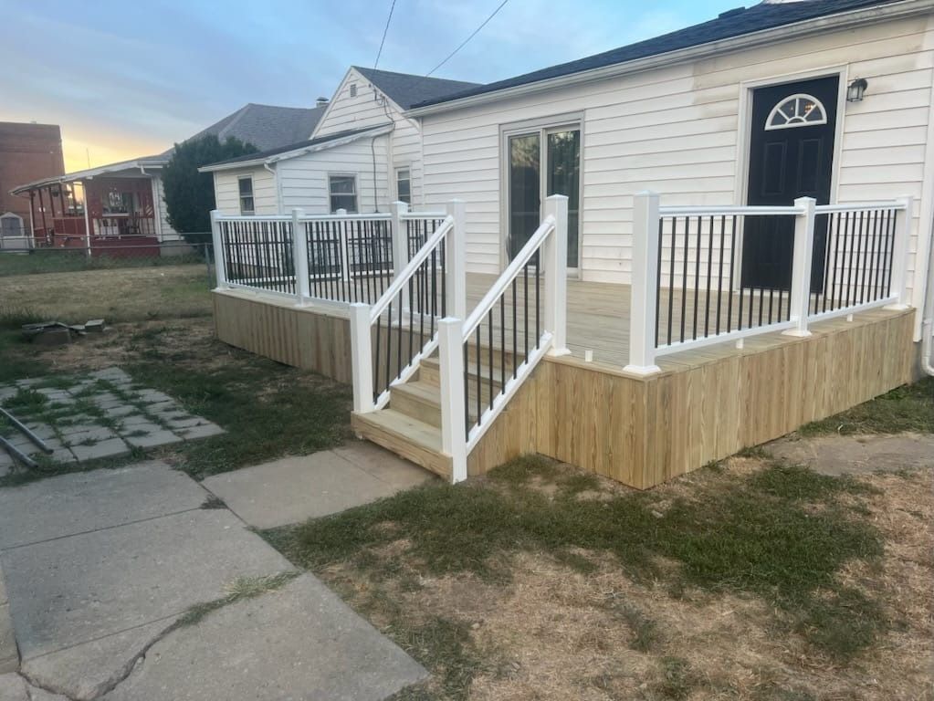 A white house with a wooden deck and stairs in front of it.