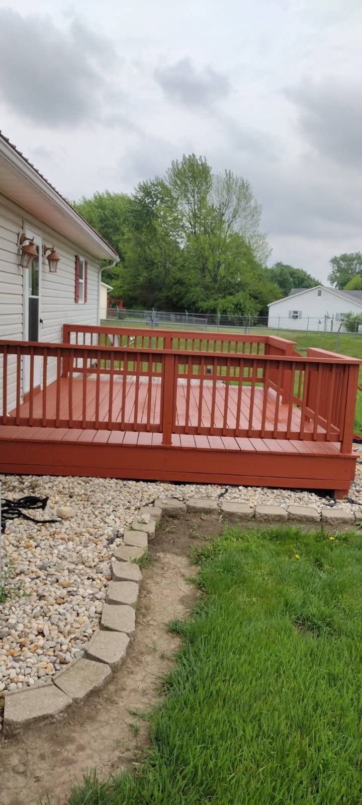 A red wooden deck is sitting in front of a white house.