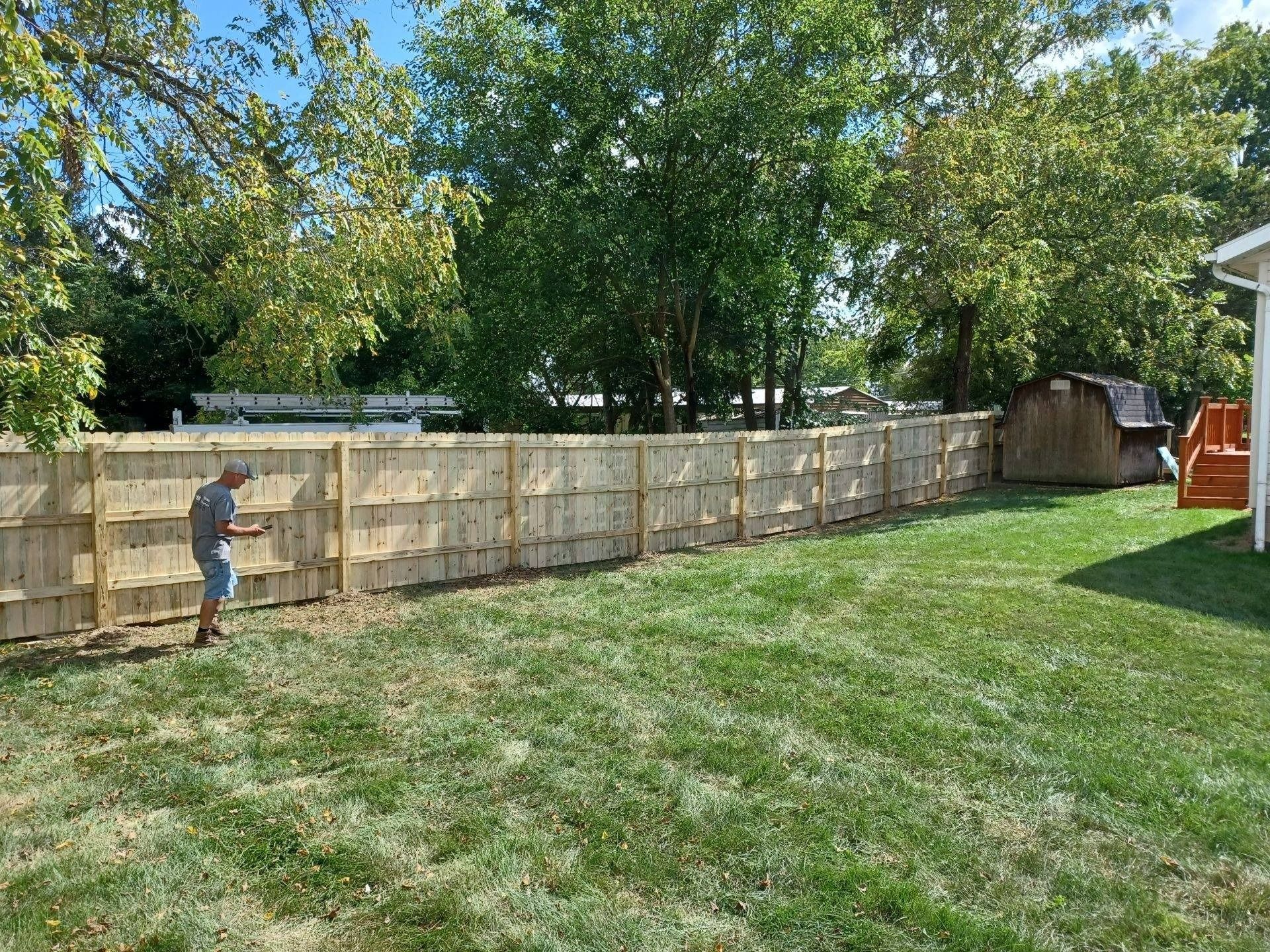 A man is standing in front of a wooden fence in a backyard.