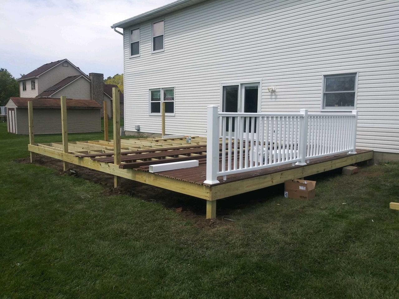 A wooden deck with a white railing is being built in front of a white house.