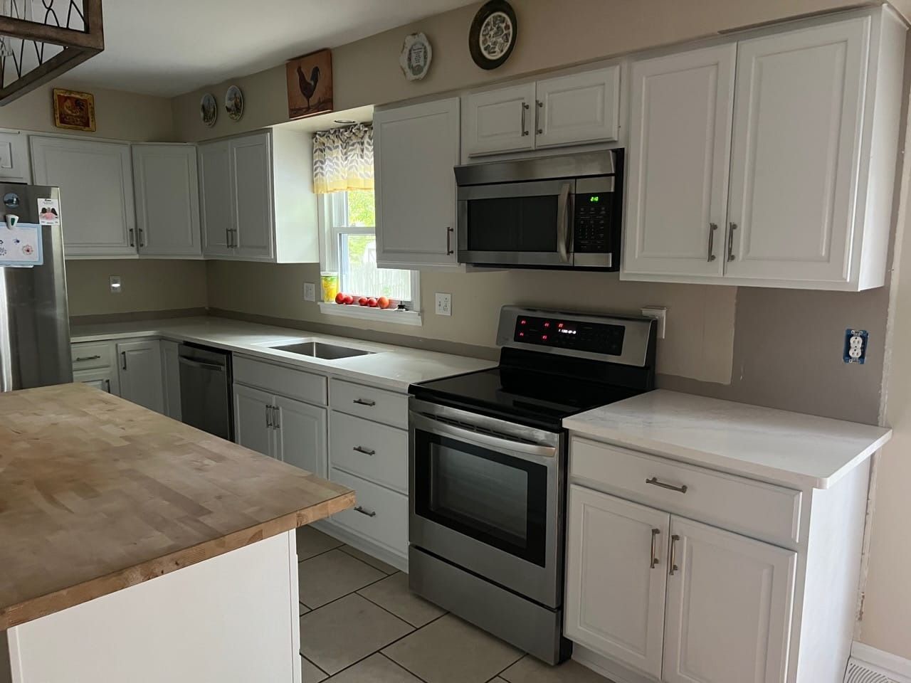 A kitchen with white cabinets , a stove , a microwave , and a sink.