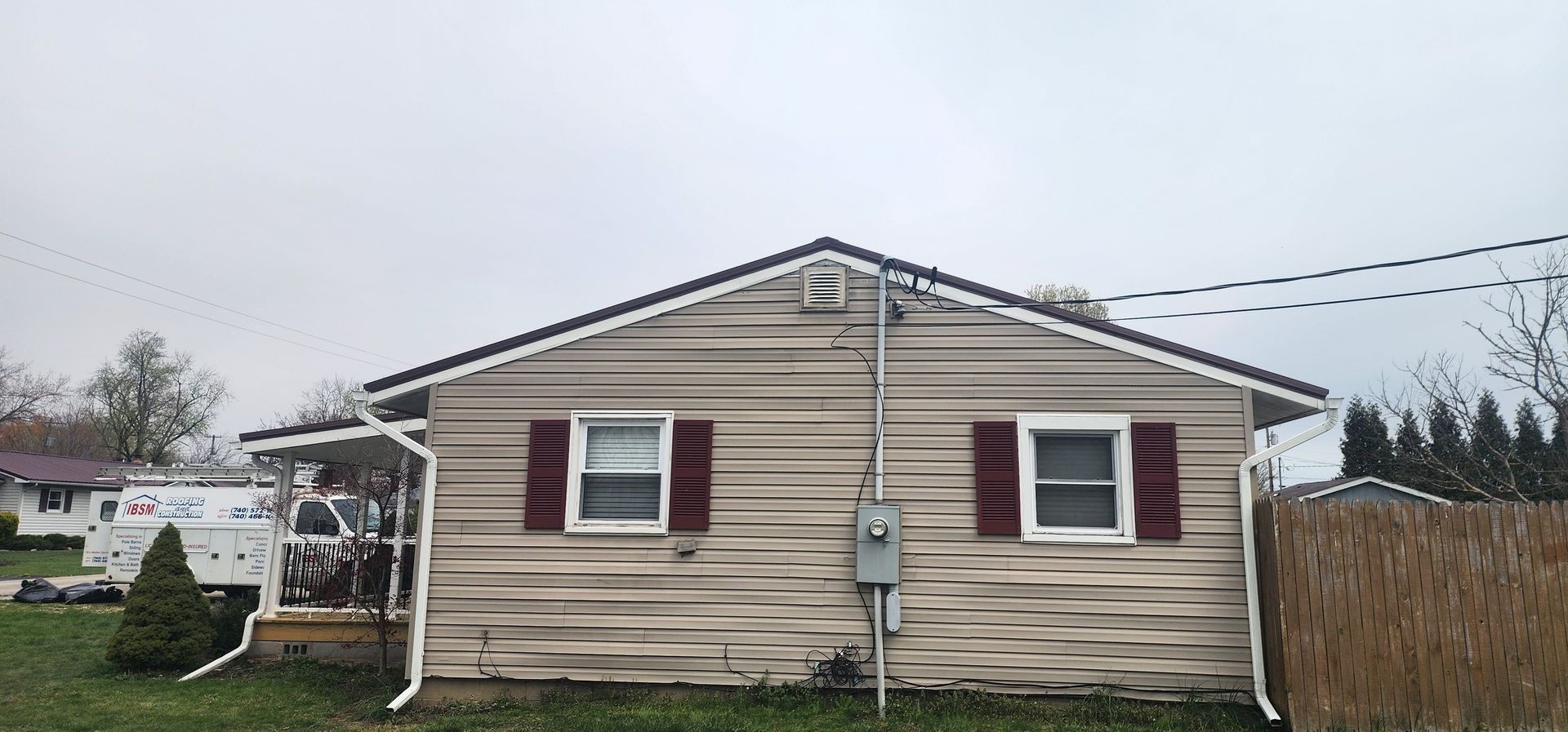 A small house with a white siding and red shutters is sitting in the middle of a grassy field.