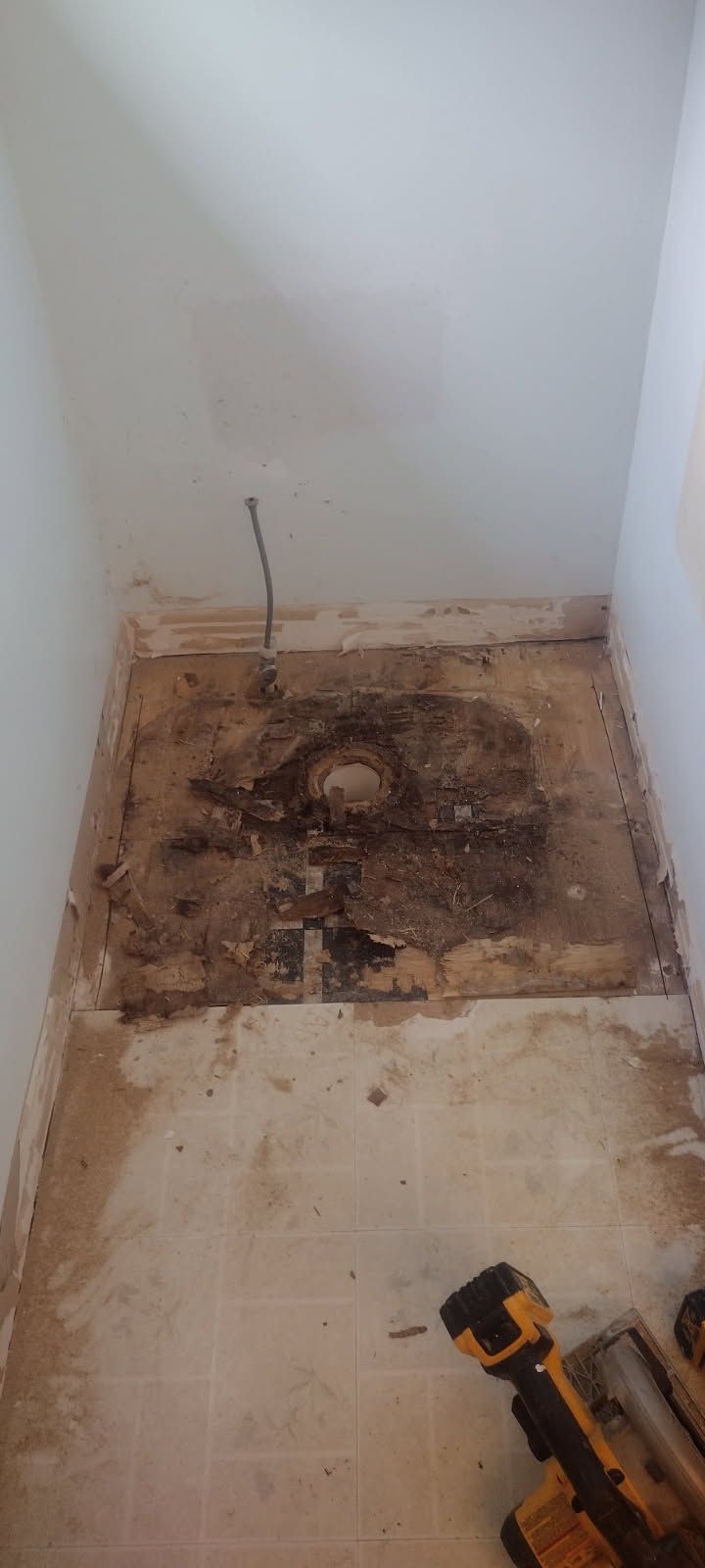 A room with a hole in the floor and a drill on the floor.