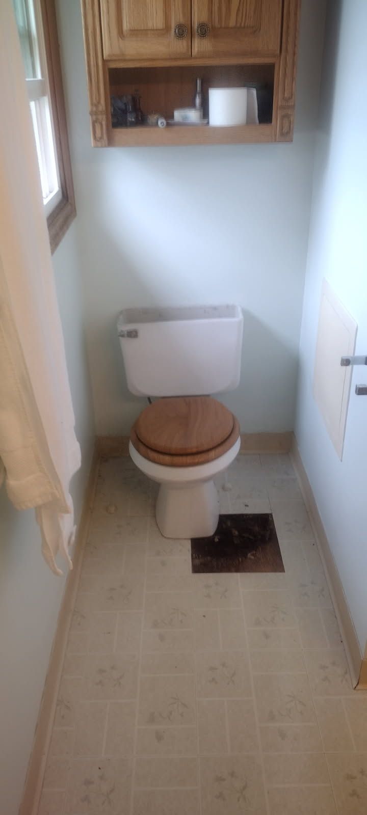 A toilet is sitting in a small bathroom next to a window.