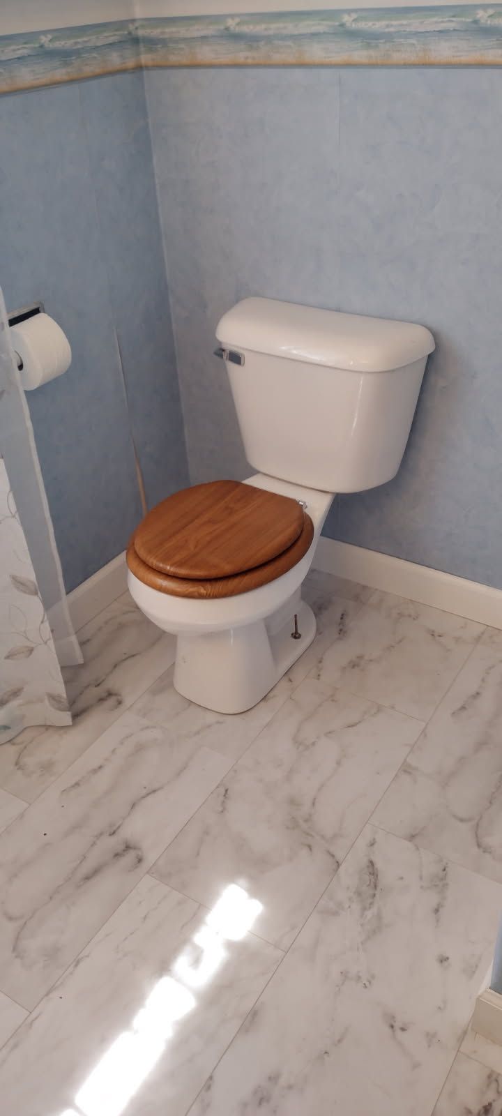 A white toilet with a wooden seat is in a bathroom.