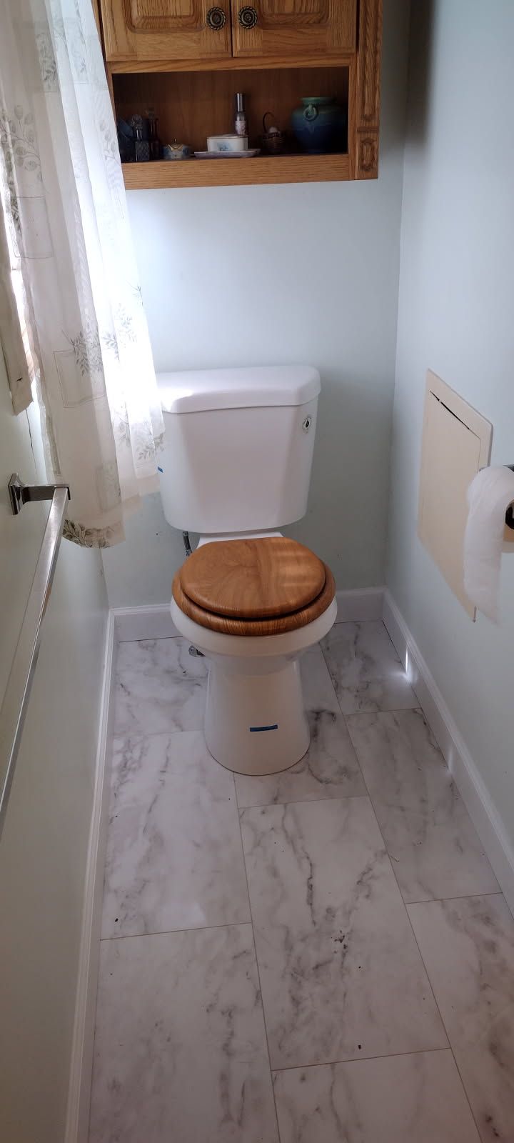 A toilet with a wooden seat is in a small bathroom.