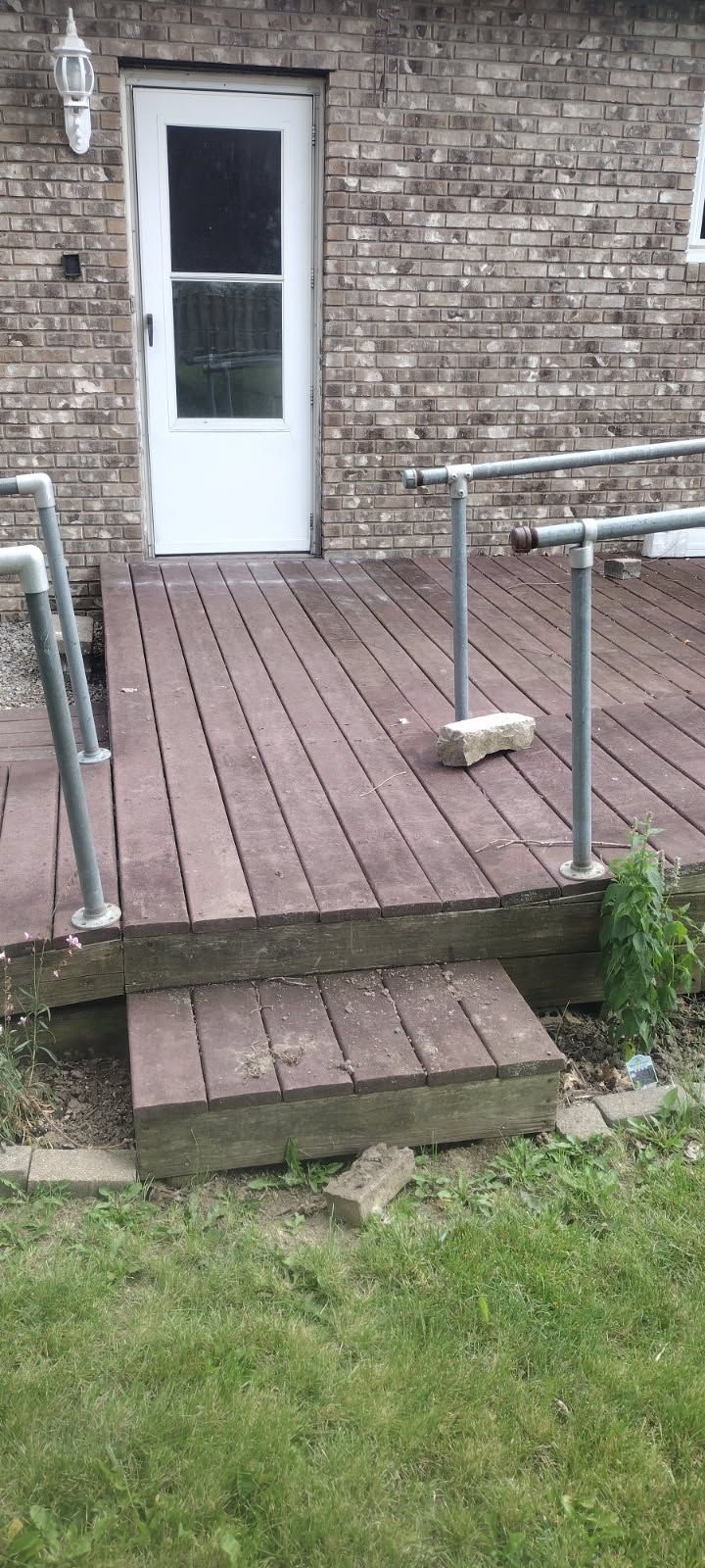 A wooden deck with a ramp leading to the door of a brick house.