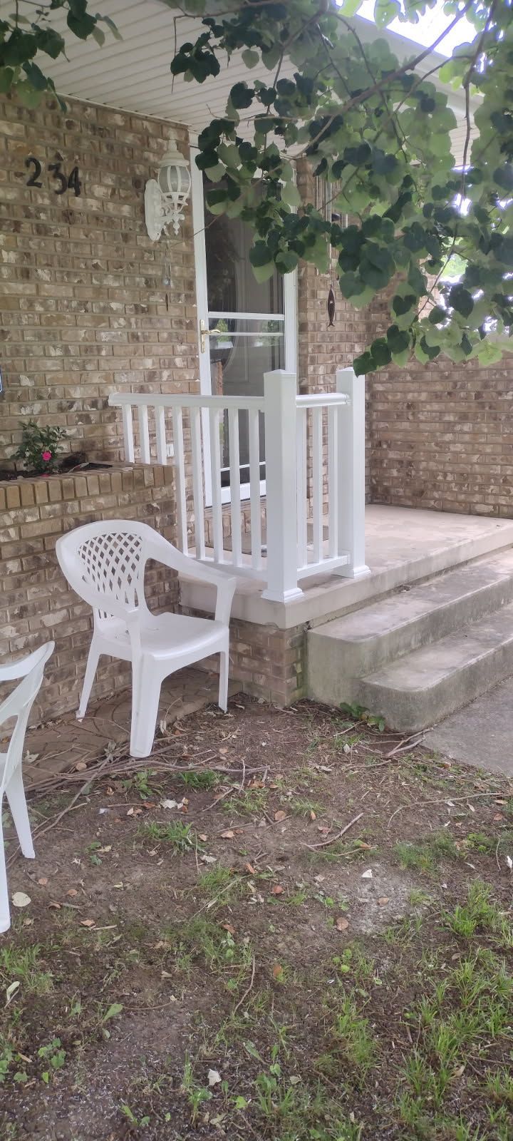 A white chair is sitting on the porch of a brick house.